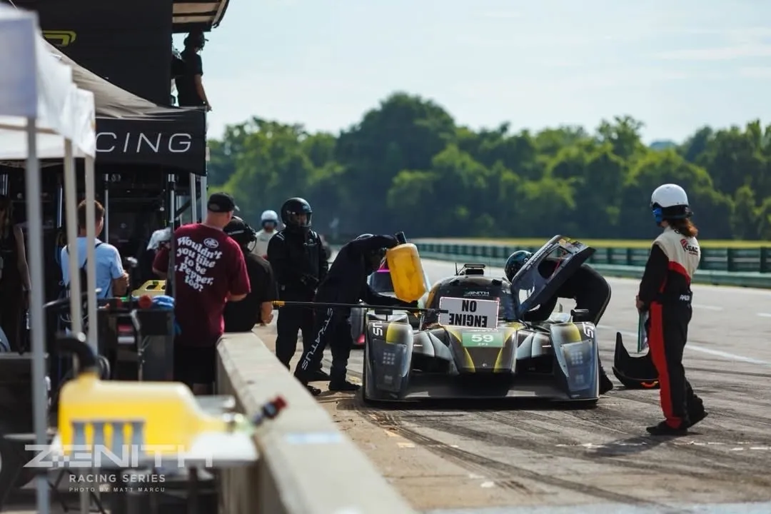 A pit stop for the #59 at VIR, crew over the car, the right-hand door up, a board reading NO ENGINE held at the wall.