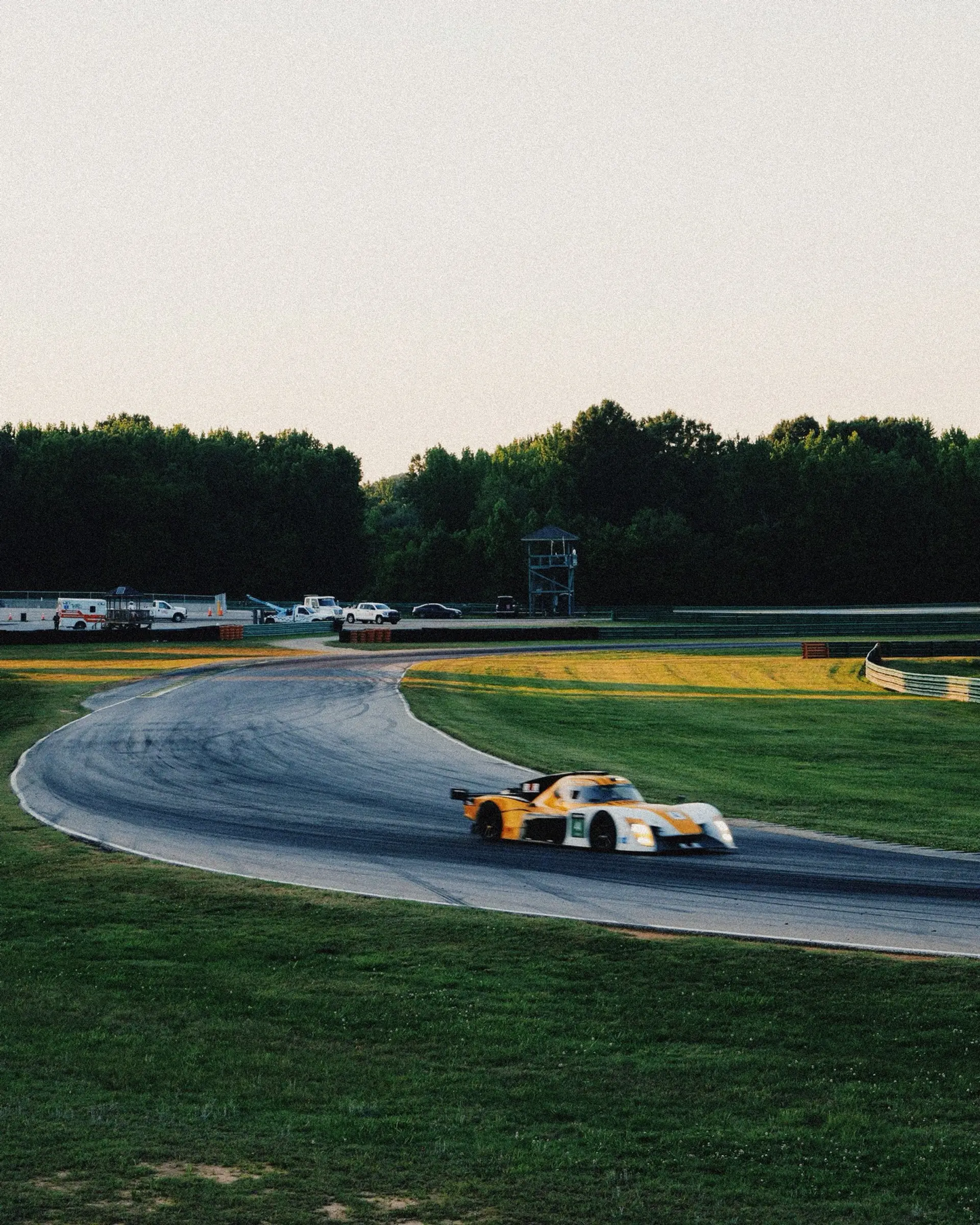 The Round 3 Racing #4 prototype on track in golden evening light, descending through a corner at VIR with the hills behind.