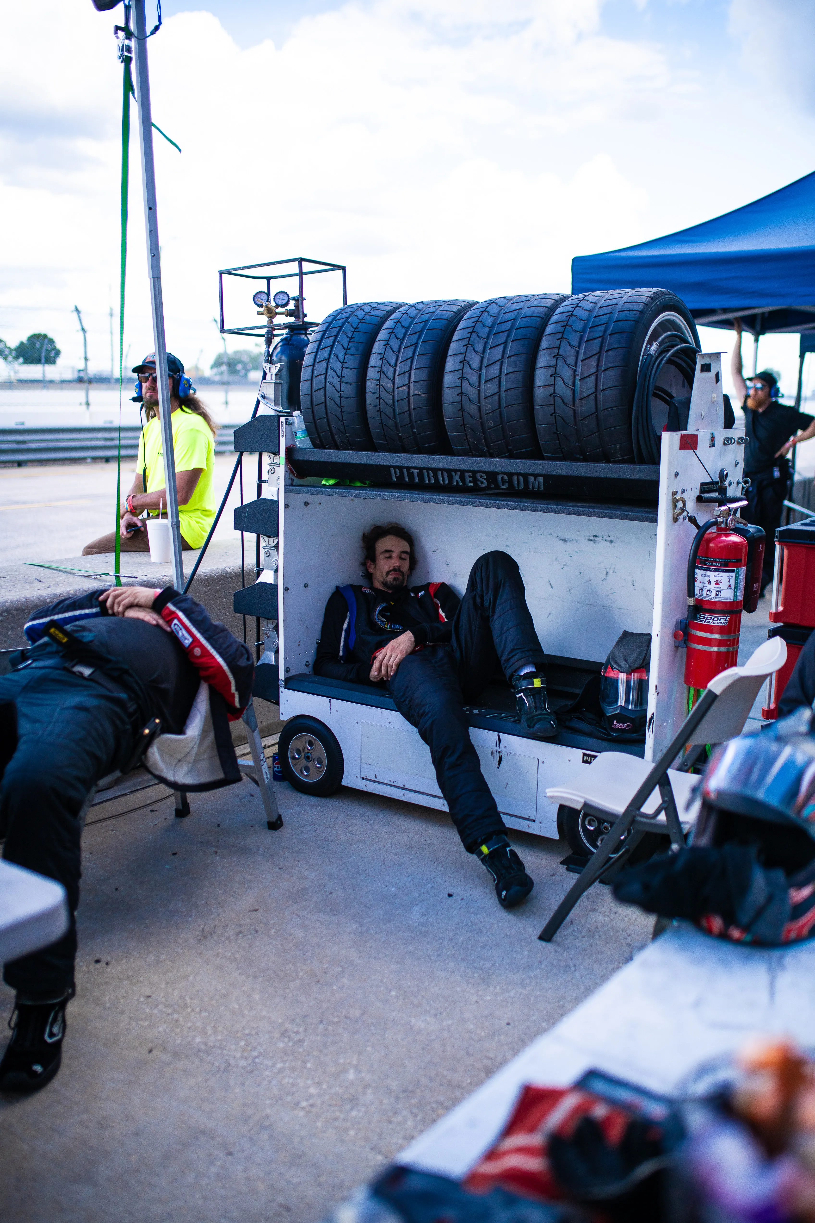 A crew member resting against the team's tire trailer between stints, the pit setup around him.
