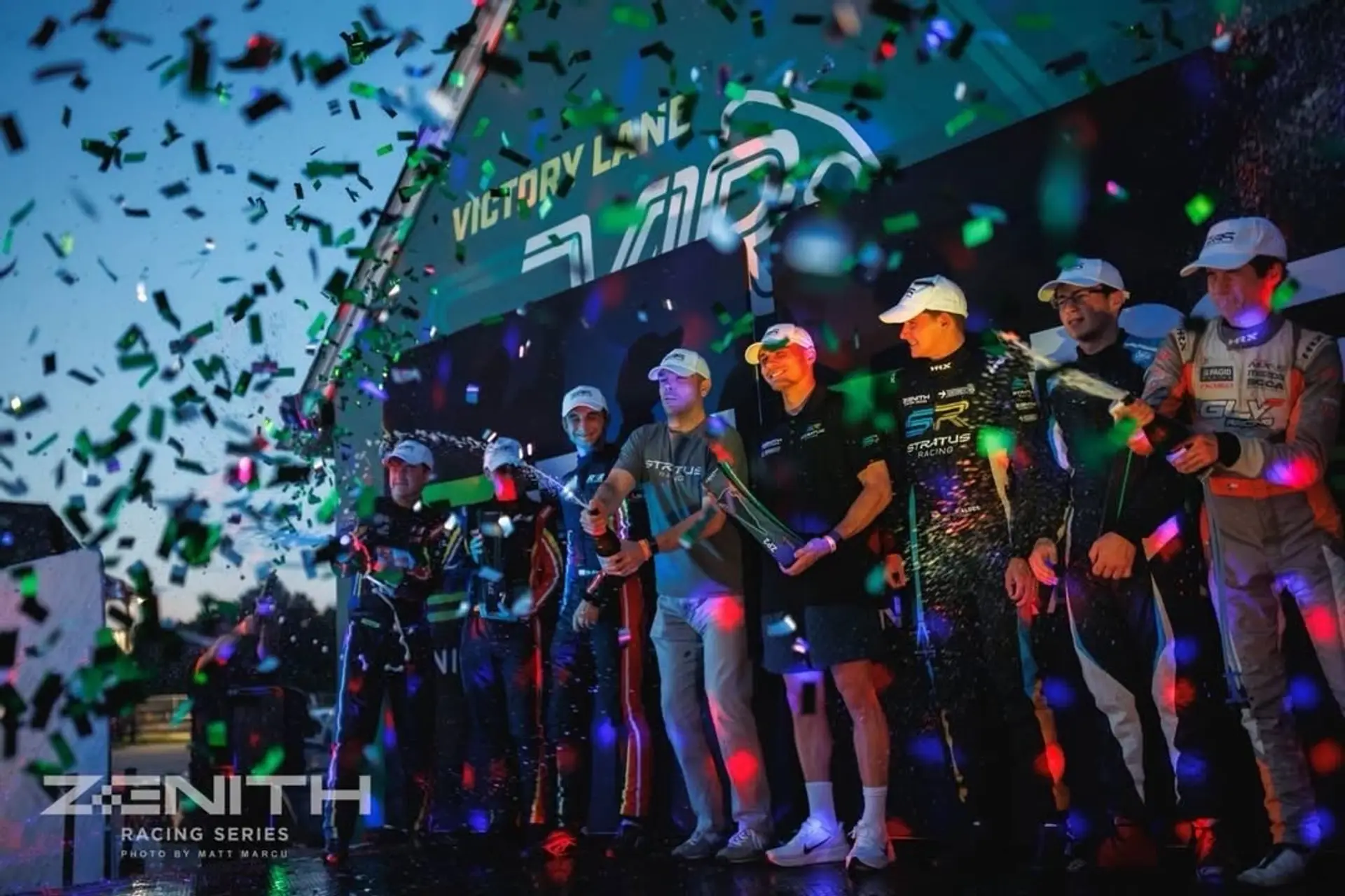 Victory Lane at VIR: the Stratus crew and drivers spraying champagne under confetti in the dusk.
