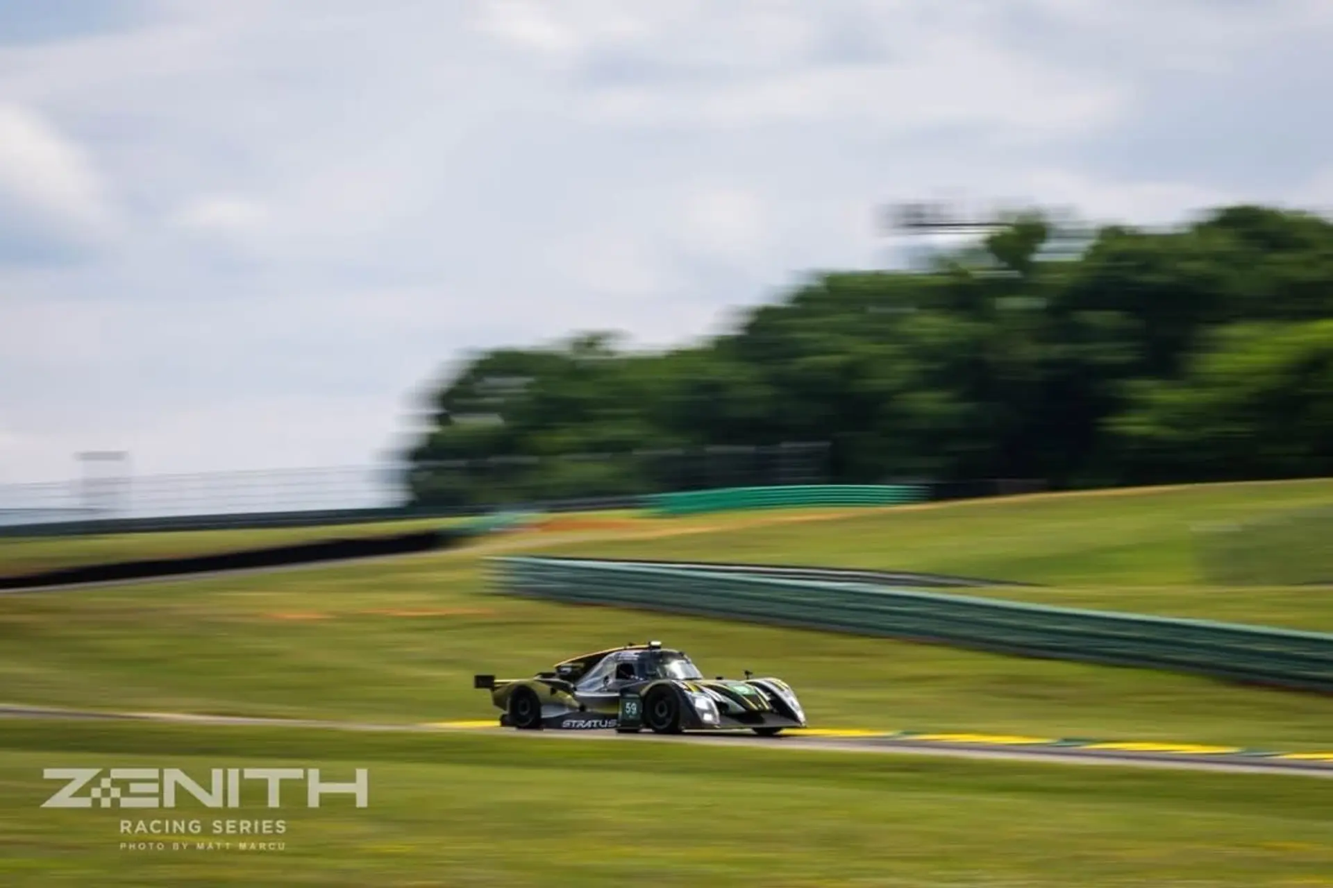 The black-and-yellow #59 Stratus prototype at speed over a crest at VIR, panned against the grass banking.