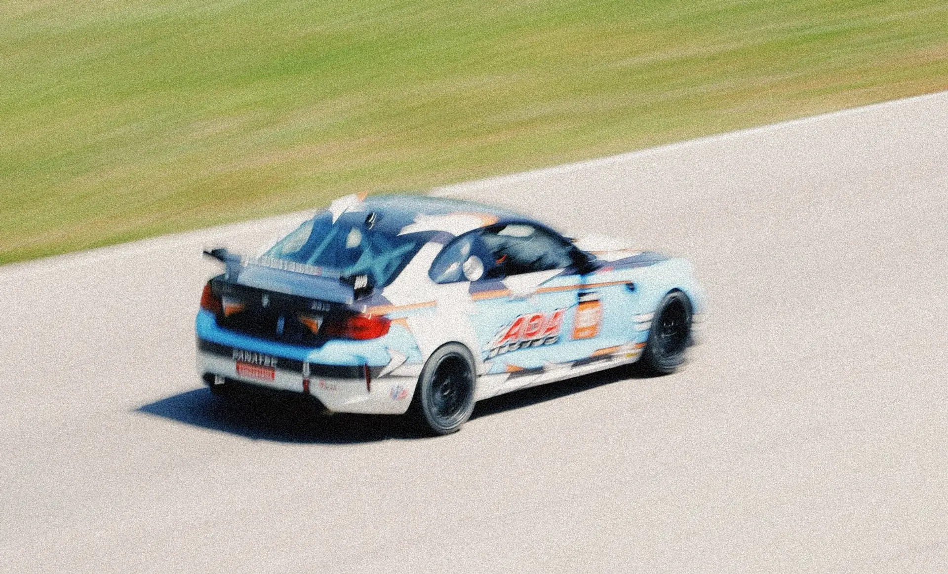 The light-blue #85 AOA Racing BMW M2 panned at speed on track at VIR, the green banking behind it.