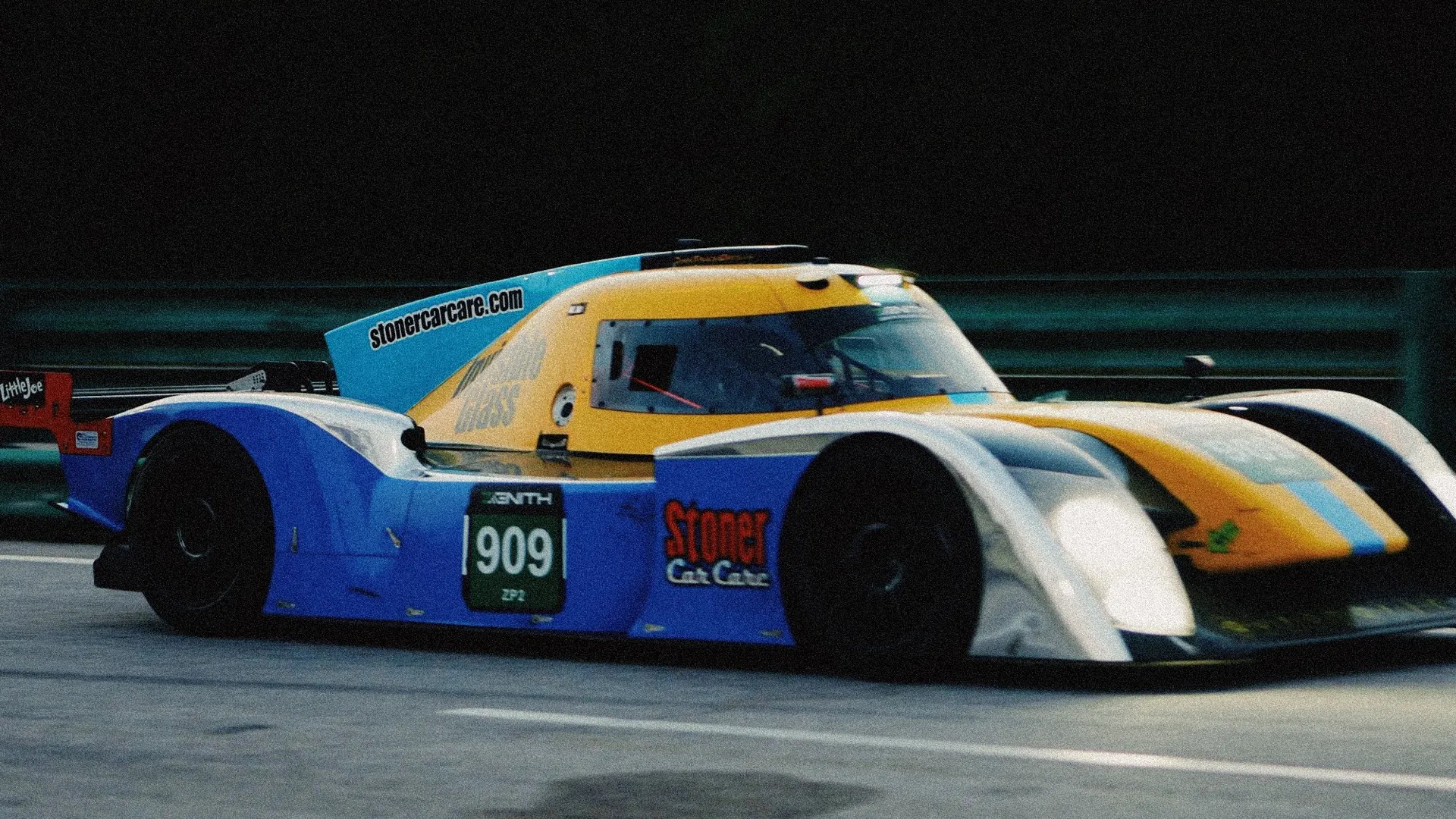 The blue-and-yellow #909 prototype at speed at VIR in fading evening light.