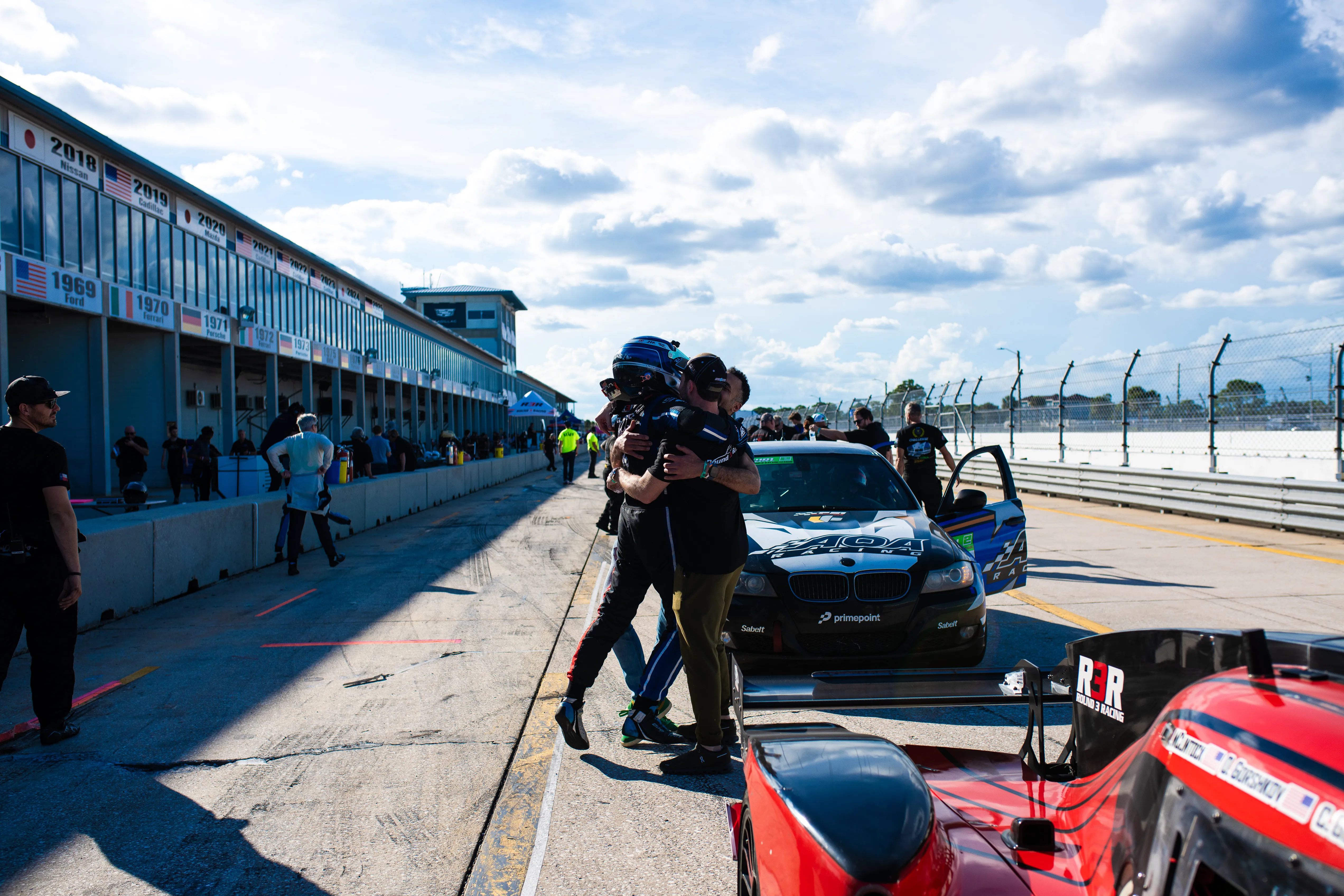 Two members of the Round 3 Racing team embrace in pit lane, the red #3 NP01 in the foreground.