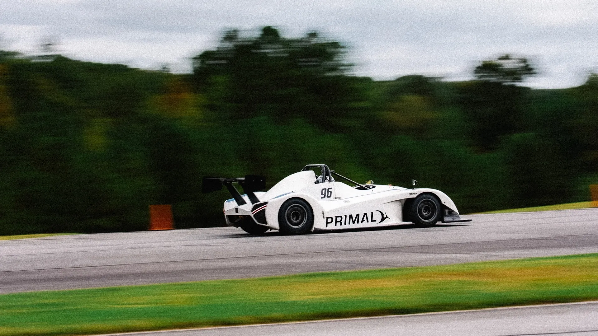 A white Primal prototype at speed on track, motion-blurred background.