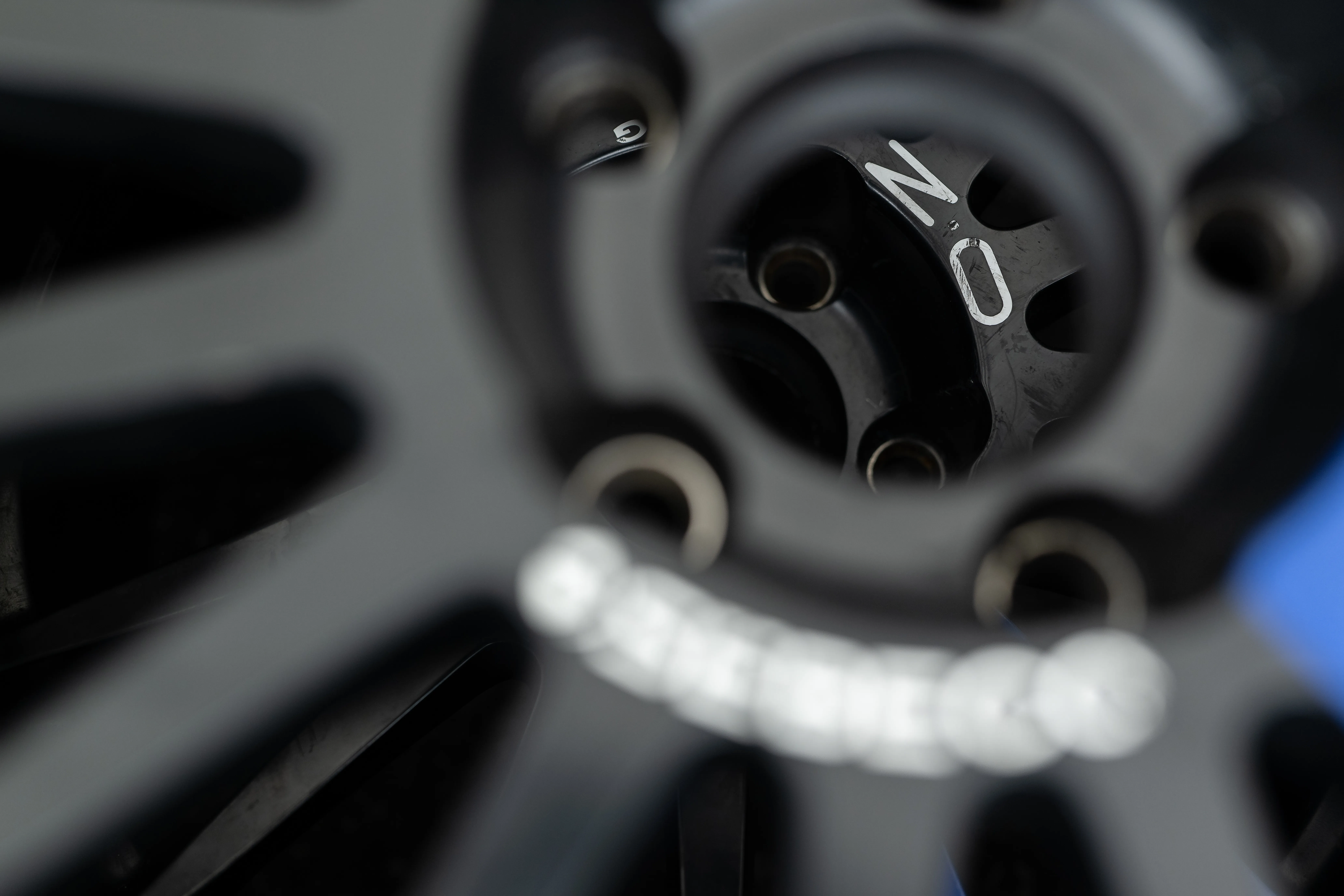 Extreme close-up of a prototype's wheel and hub, shallow focus, a tire-warmer strap visible behind.