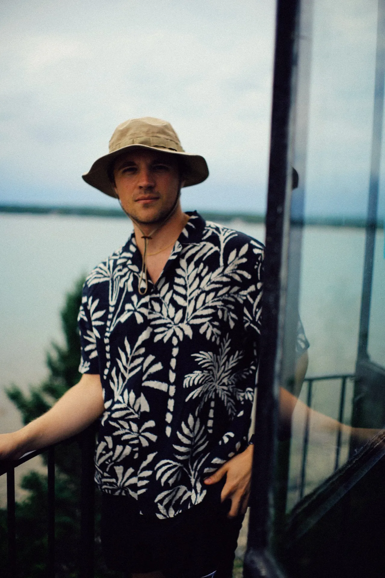 Randy Kinne in a bucket hat and palm-print shirt, leaning on a railing by the water.