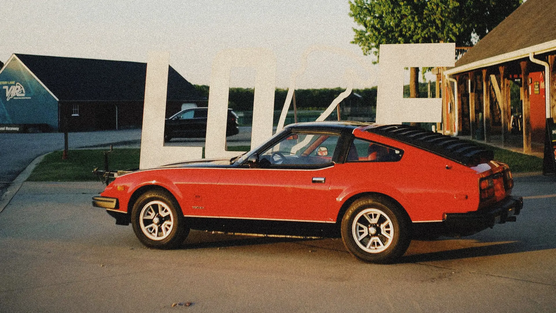 A classic red sports car parked in warm golden light in front of the large white VIR letters at the circuit entrance.