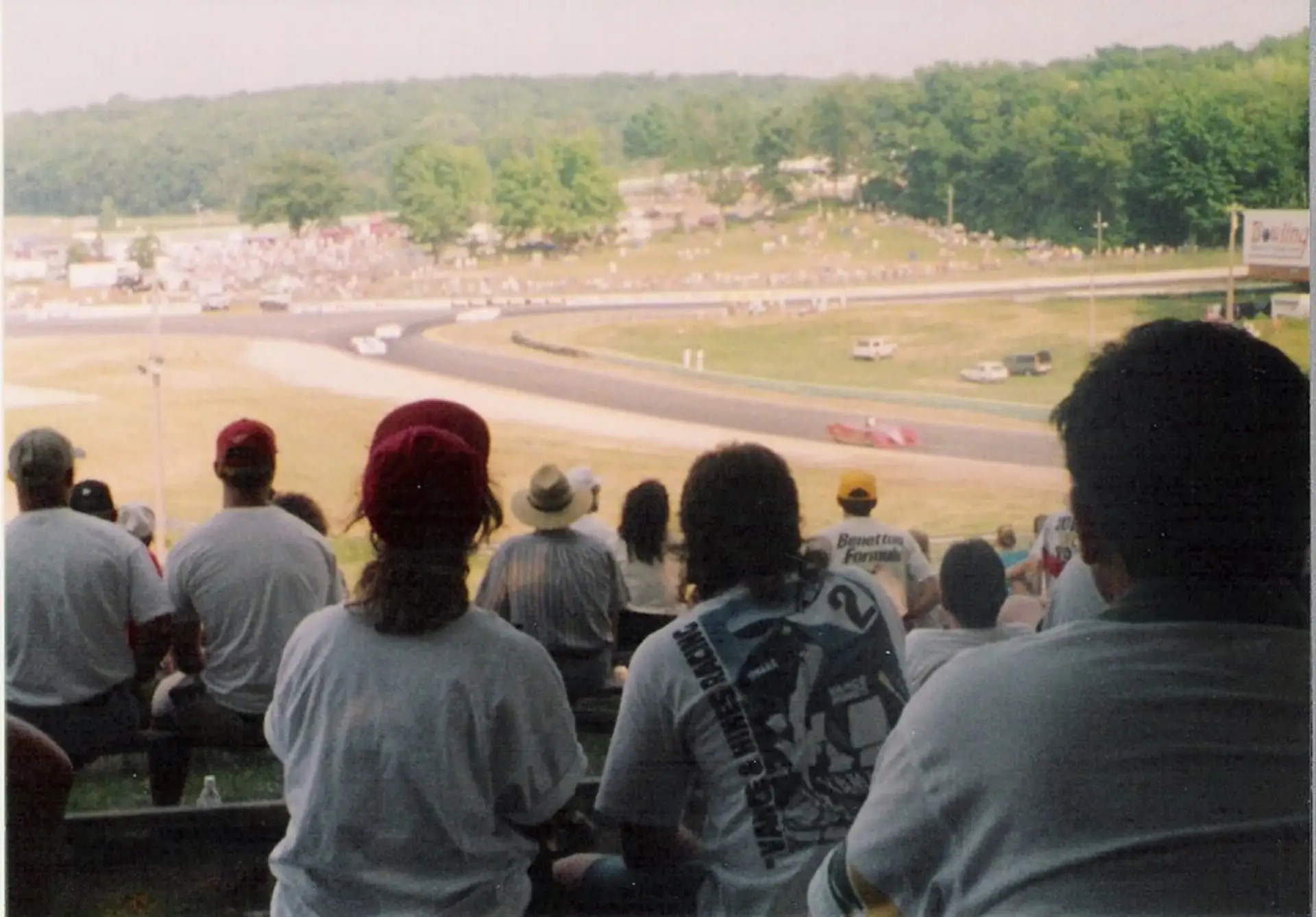 Spectators on a grassy hillside watching cars sweep through a corner, an older photograph.