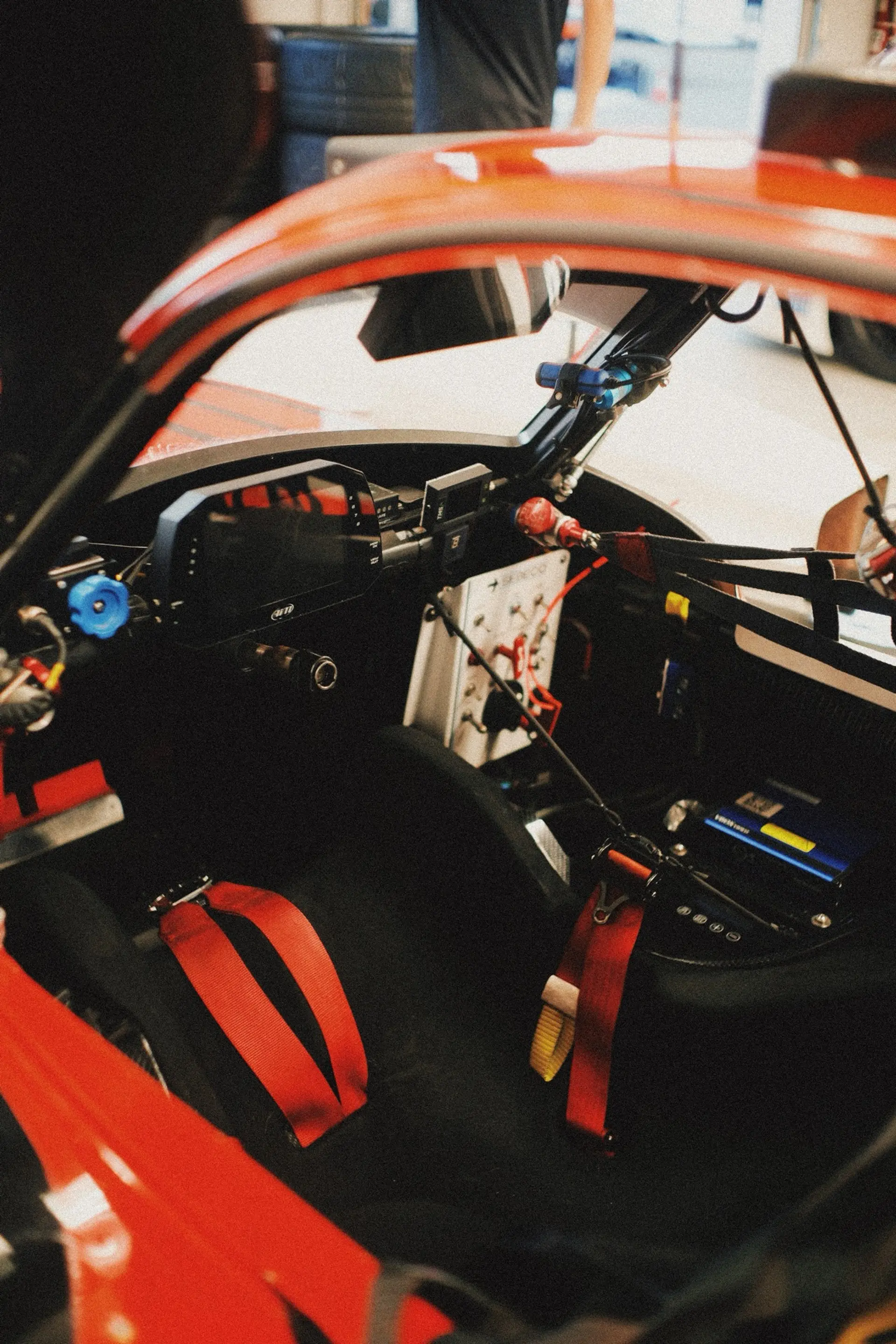 A driver sealed into a prototype cockpit, helmet on and hands on the wheel, seen through the side window.