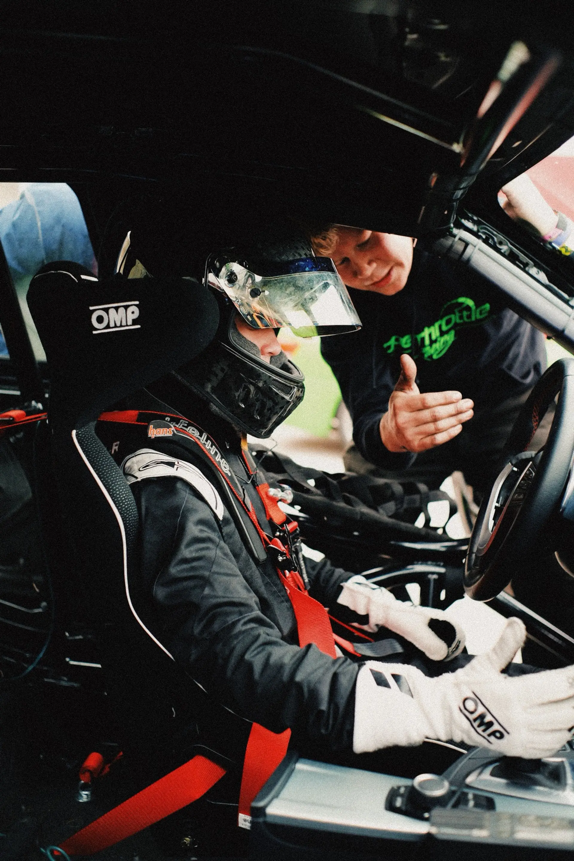 The handoff, up close: a driver sealed in, a crew member leaning through the window with the last word before the belts come tight. The driver change is what makes endurance racing a team sport.