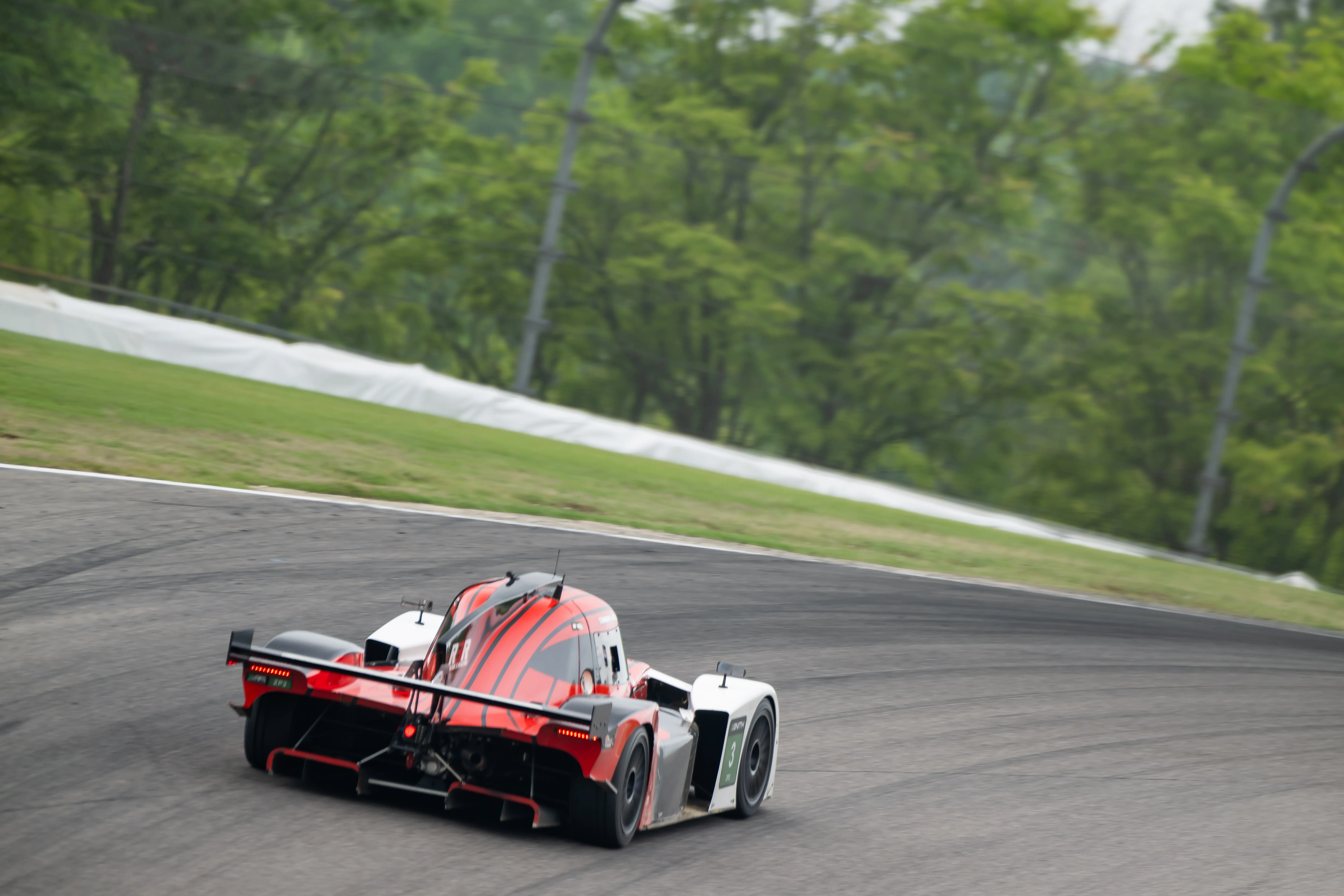 The red #3 Round 3 Racing NP01 going away up the track, woods behind.