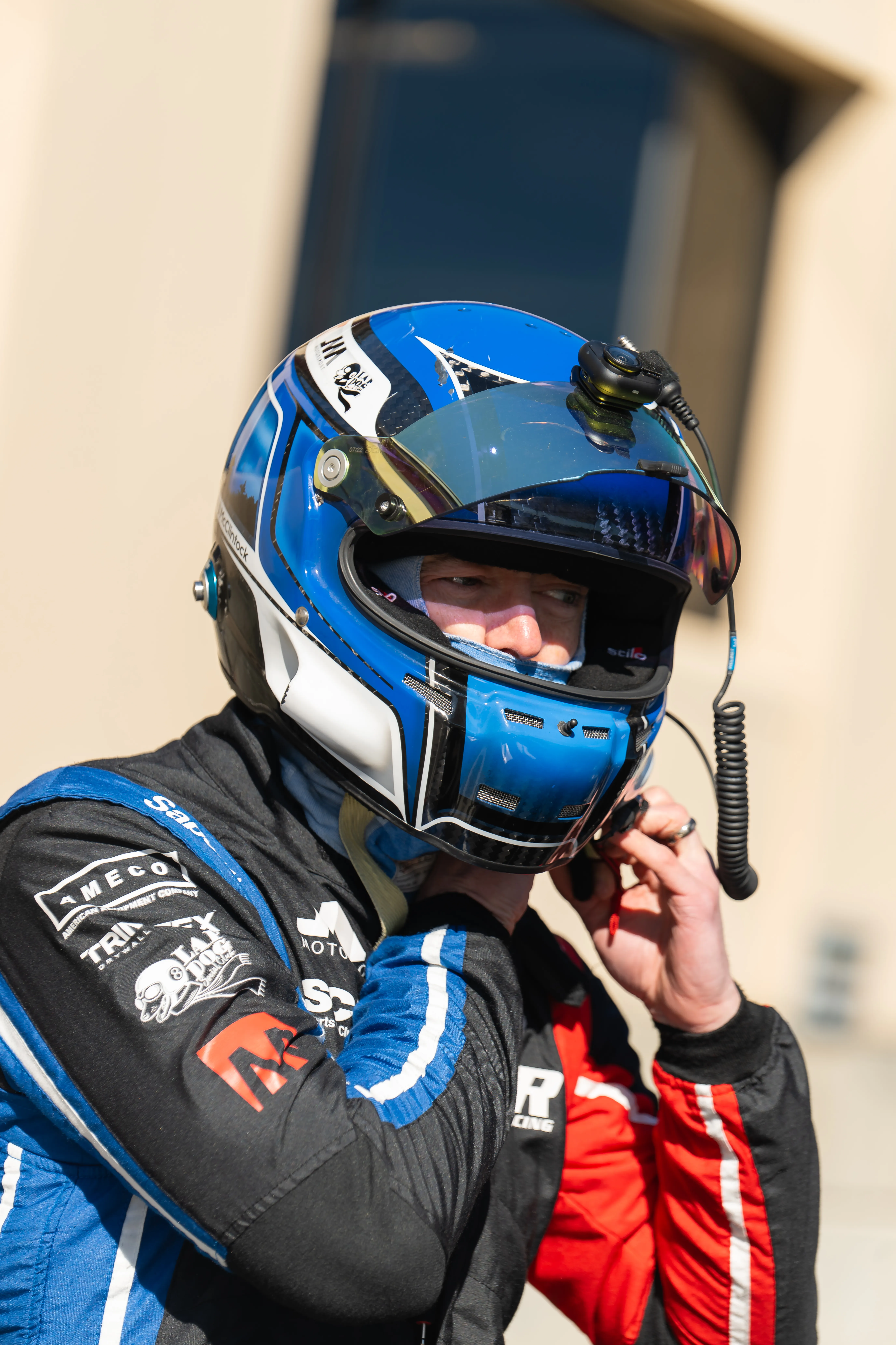 Jon McClintock in his blue-and-black helmet, visor up, adjusting his radio between sessions.