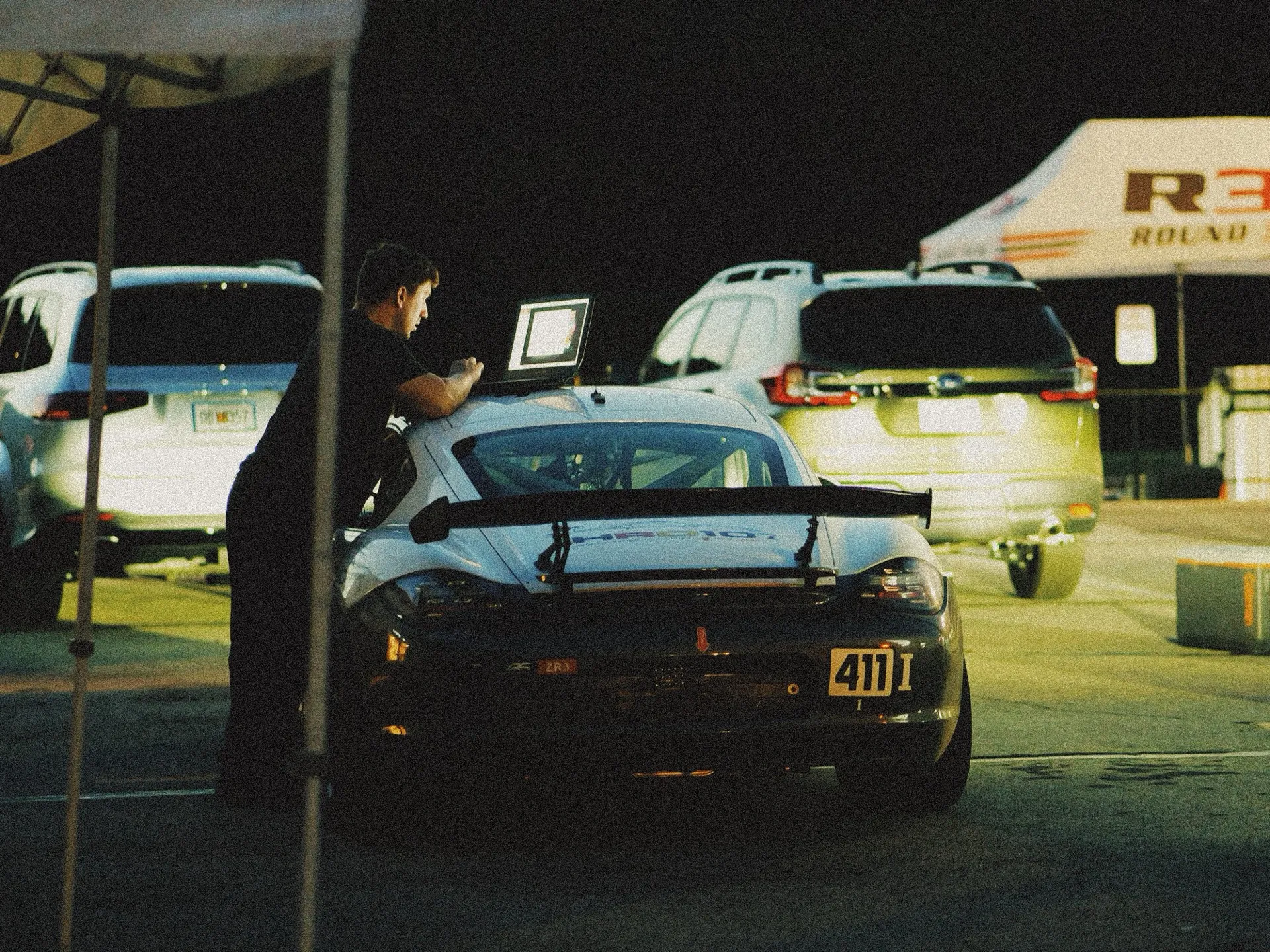 A GT car being worked on under a tent at night at VIR, a laptop open on the rear wing.