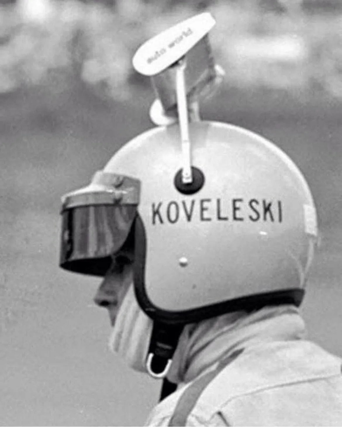 Oscar Koveleski in profile, wearing an open-face helmet with a small aero wing mounted on top labeled 'Auto World.'