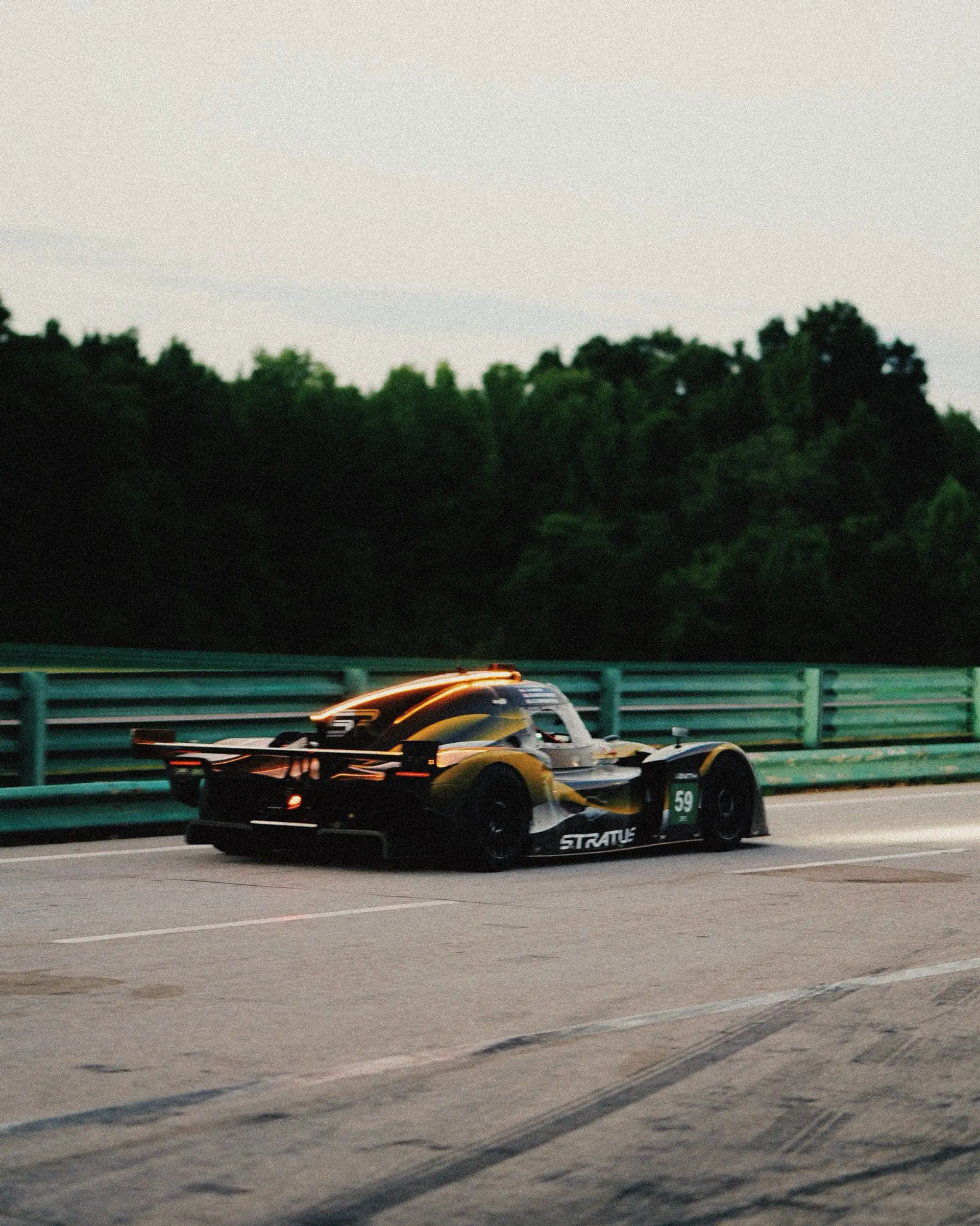 A yellow-and-black prototype on track at dusk at VIR, the tree line dark against a fading sky.